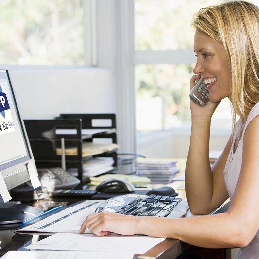 Woman in home office with computer using telephone smiling