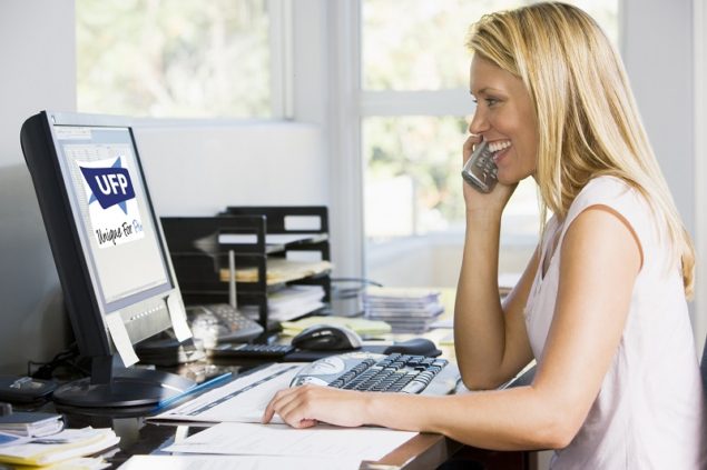 Woman in home office with computer using telephone smiling